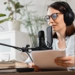 caucasian-millennial-woman-with-a-microphone-and-headphones-recording-a-podcast-in-a-recording-studio